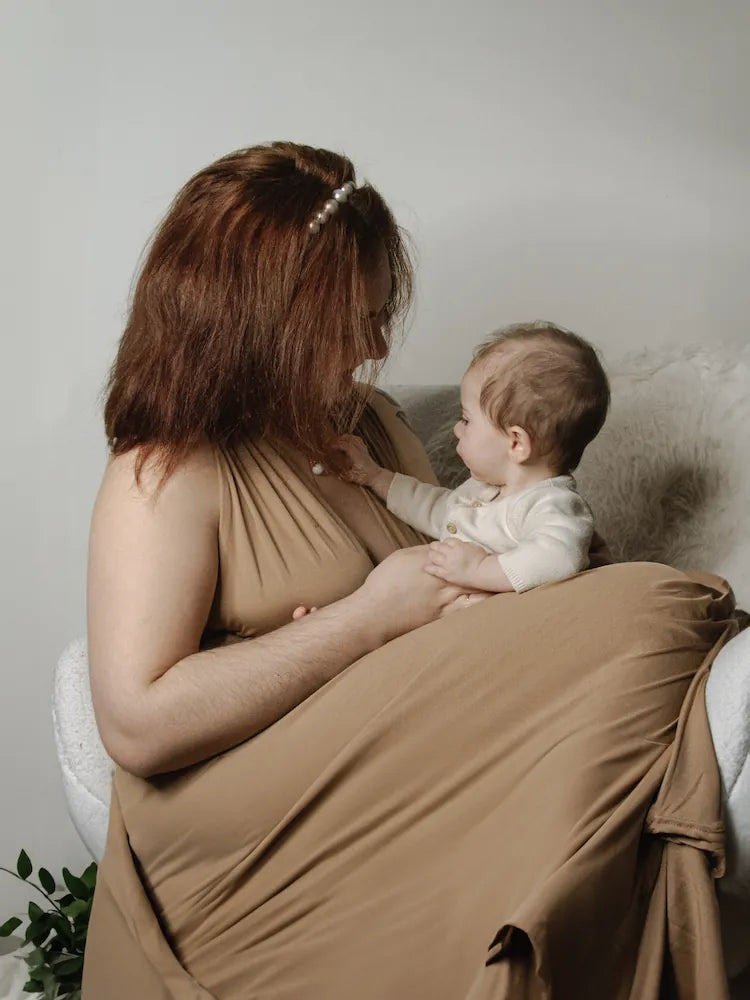 Woman in a brown dress holding a baby in a neutral setting