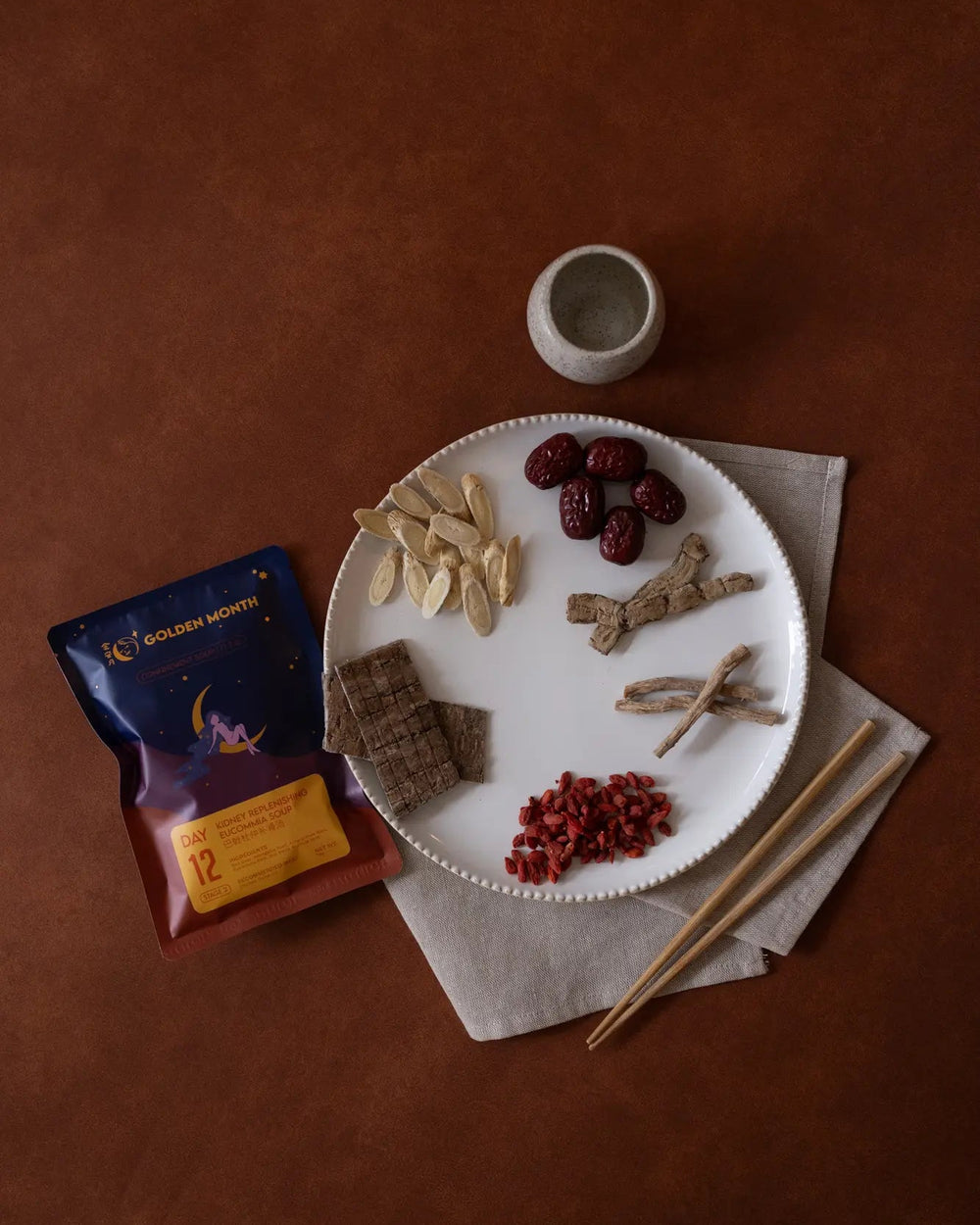 Dried fruits and nuts on a plate with a package of Golden Harvest tea on a brown surface.