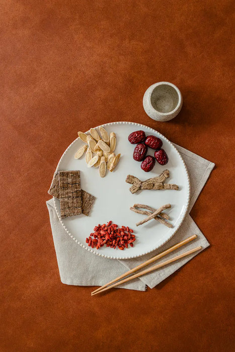 Assorted confinement  herbs and nuts on a white plate with chopsticks on a brown surface