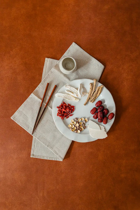 Dessert plate with Chinese traditional herbs, and a small cup on a brown surface.