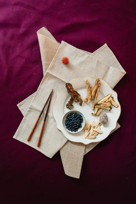 Dried confinement herbs on a plate with chopsticks and a bowl of blackberries on a purple background