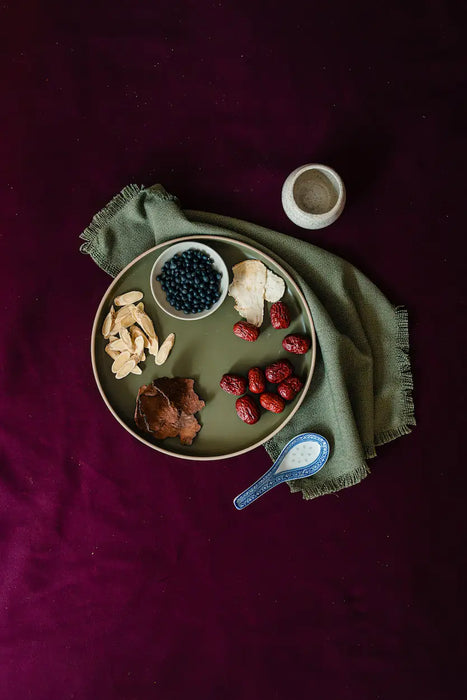 Assorted dried fruits and confinement herbs on a plate with a green napkin on a dark surface