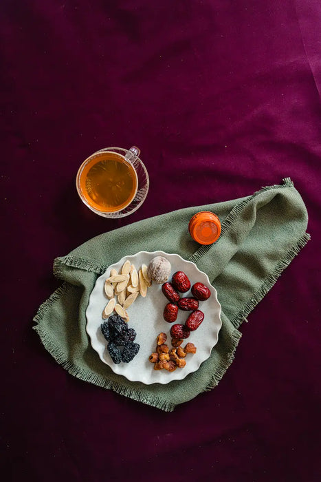Dried herbs on a plate with a cup of tea on a green cloth against a purple background