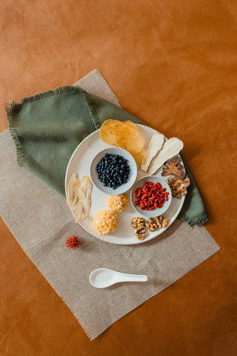 Assorted confinement herbs on a plate with a spoon on a textured surface