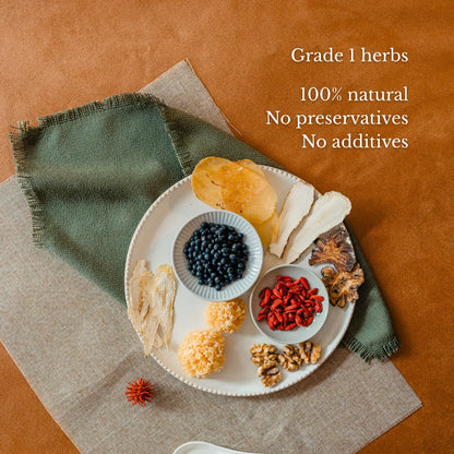Assorted dried herbs on a white plate with a green napkin on a brown surface, labeled as grade 1 herbs with natural and additive-free qualities.
